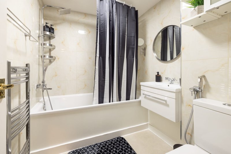 Modern bathroom with white bath, striped shower curtain, mirror and sink vanity