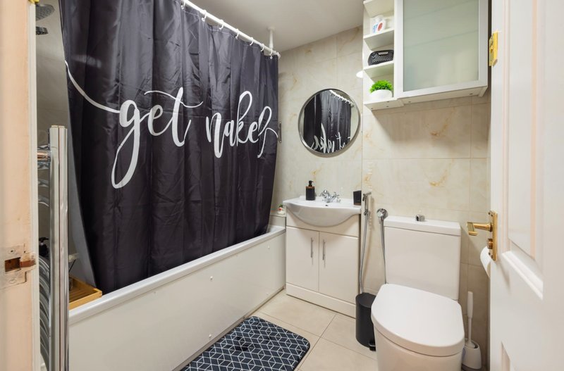 Bathroom with white toilet, sink, mirror, and black shower curtain with text