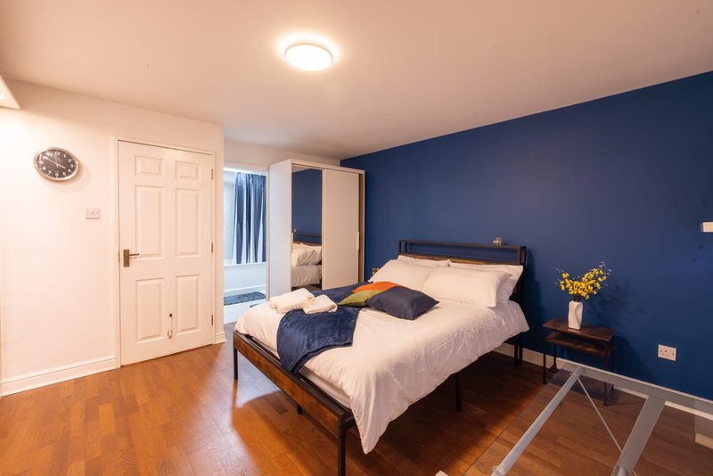 Bedroom with double bed, navy blue accent wall, wooden floor and white wardrobe