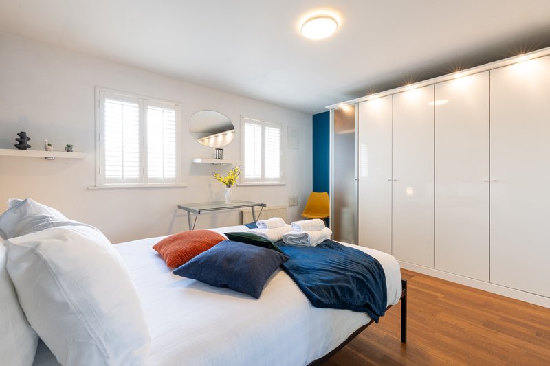 Bright modern bedroom with double bed, navy and orange pillows, wooden floor, and white built-in wardrobe