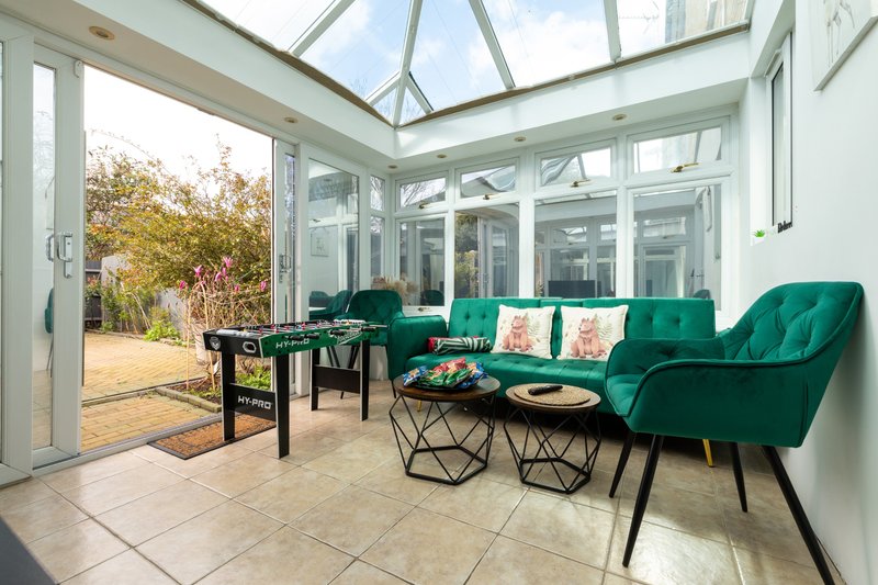Bright conservatory with green armchairs, glass roof, garden view and tiled flooring