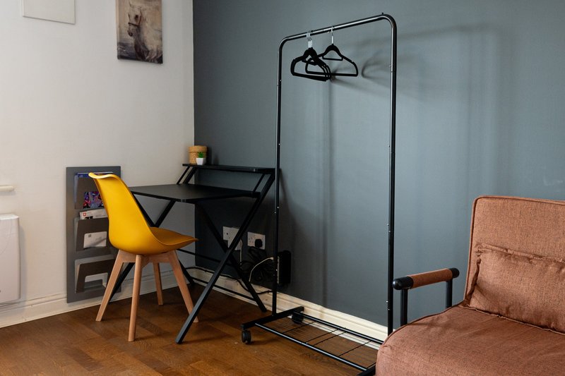 Modern bedroom with desk, yellow chair, clothing rack, and brown armchair