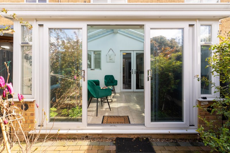 Modern conservatory with glass doors, green chairs, and garden views through windows