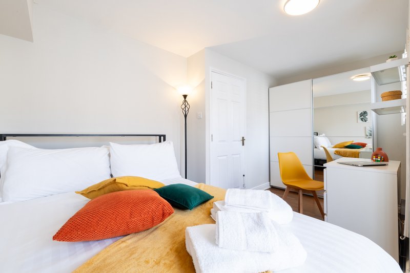 Bright modern bedroom with double bed, colorful cushions, mirrored wardrobe and desk area