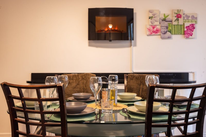 Modern dining room with black table, two chairs, place settings, and wall-mounted fireplace