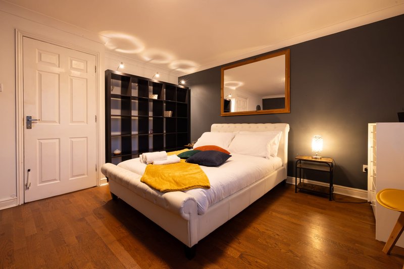 Modern bedroom with white bed, dark accent wall, mirror, shelving unit and wooden floor