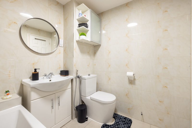 Modern bathroom with circular mirror, white vanity, toilet, and patterned floor mat