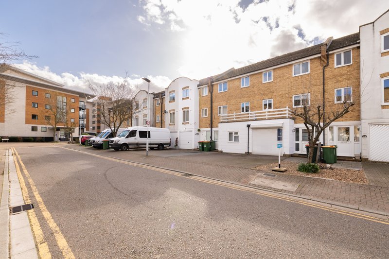 Residential street with brick apartment buildings, parked vehicles, and paved courtyard area