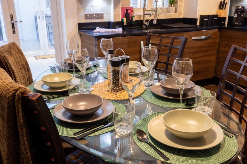 Dining table set for meal with place settings, glassware, and open kitchen in background