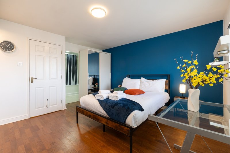 Modern bedroom with double bed, deep blue accent wall, yellow flowers, and wooden flooring
