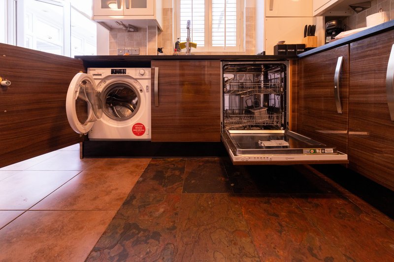 Modern kitchen with open wooden cabinets, washing machine, dishwasher and terracotta floor