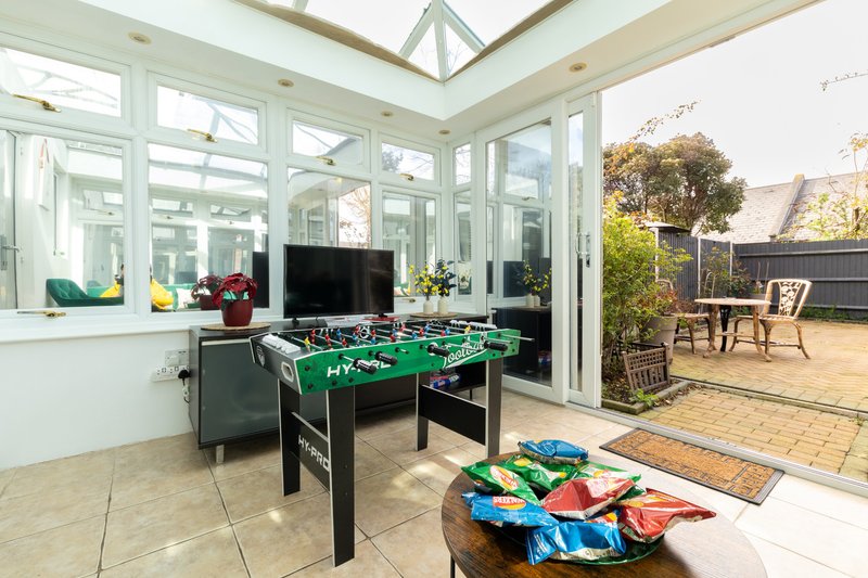 Bright conservatory with foosball table, patio doors, and garden access with seating area