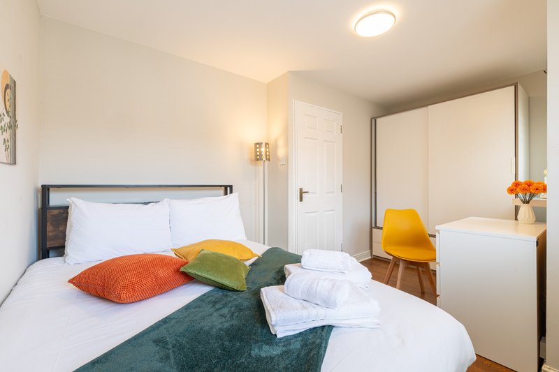 Bright bedroom with double bed, colorful pillows, folded towels, yellow chair and mirror