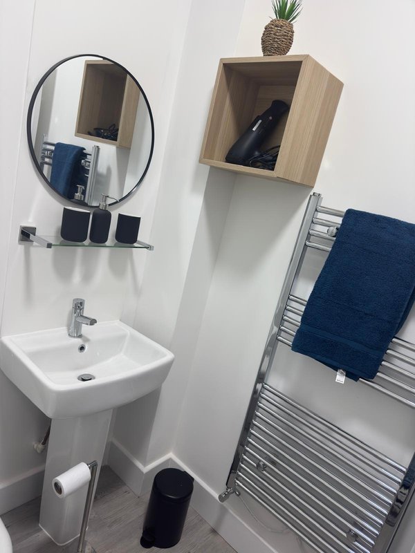 Modern bathroom with round mirror, white sink, towel rail and wooden shelf with plant
