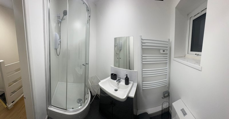 Modern bathroom with curved shower cubicle, white sink, heated towel rail and storage.