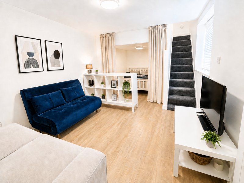 Open-plan living room with blue velvet sofa, cream armchair, TV, wooden flooring and stairs