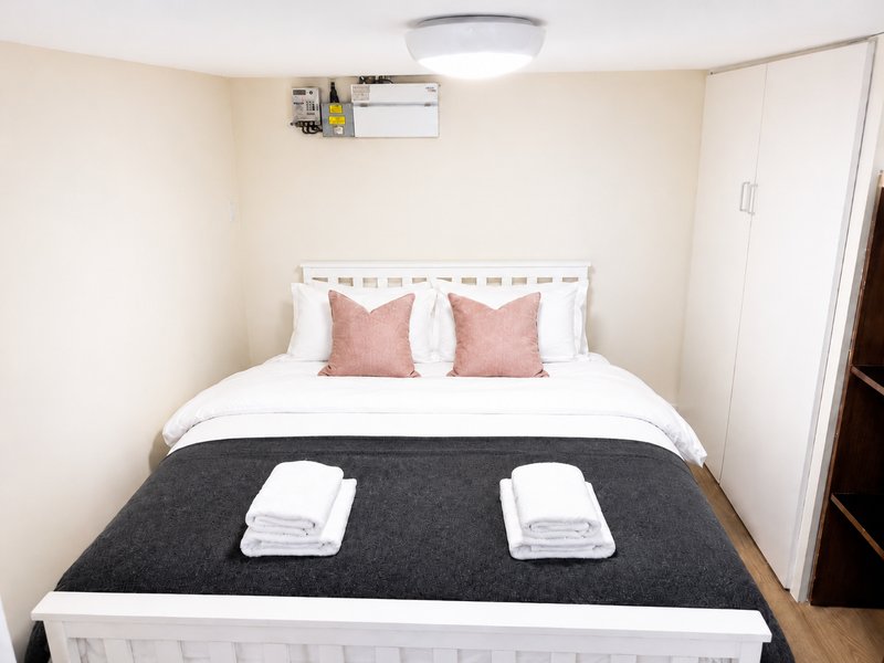 Small bedroom with double bed, pink cushions, white headboard and folded towels