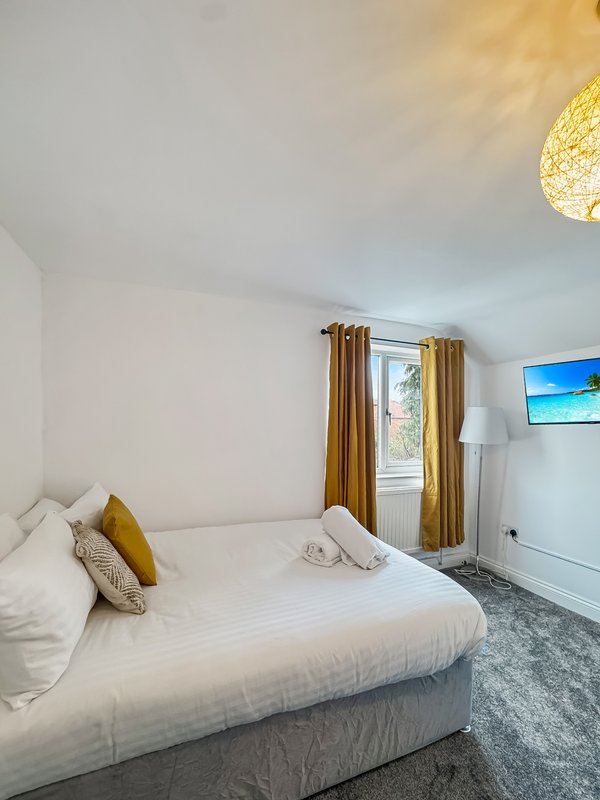 Bright bedroom with double bed, white bedding, gold curtains and pendant light