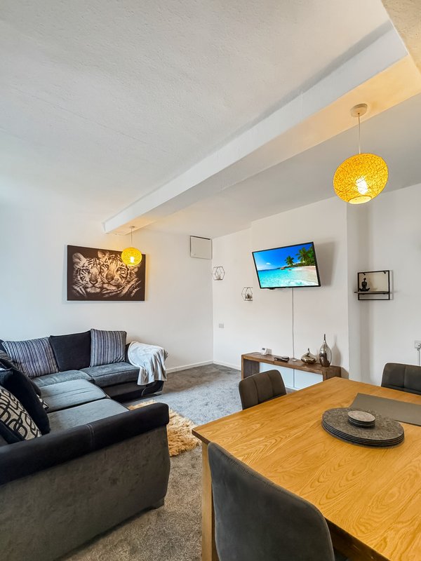 Modern open-plan living room with black sofa, wooden dining table, wall-mounted TV and yellow pendant lighting