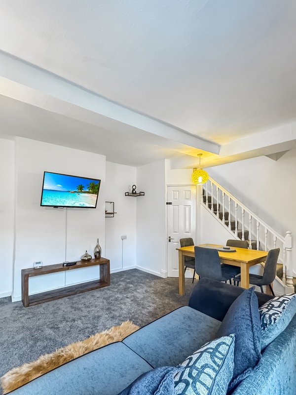 Open-plan living area with blue sofa, wall-mounted TV, wooden console table, dining table and stairs