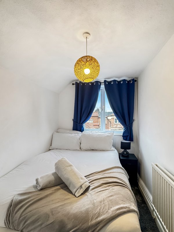 Bedroom with single bed, gold pendant light, navy curtains and window view