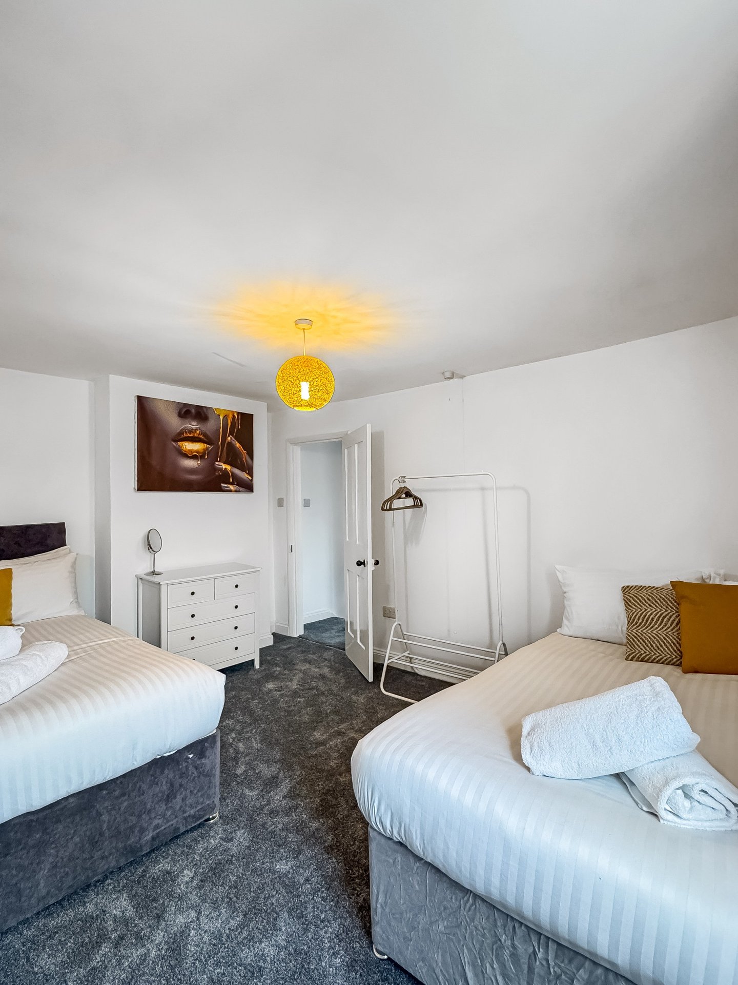 Twin bedroom with two single beds, white dresser, yellow ceiling light, and ensuite shower area
