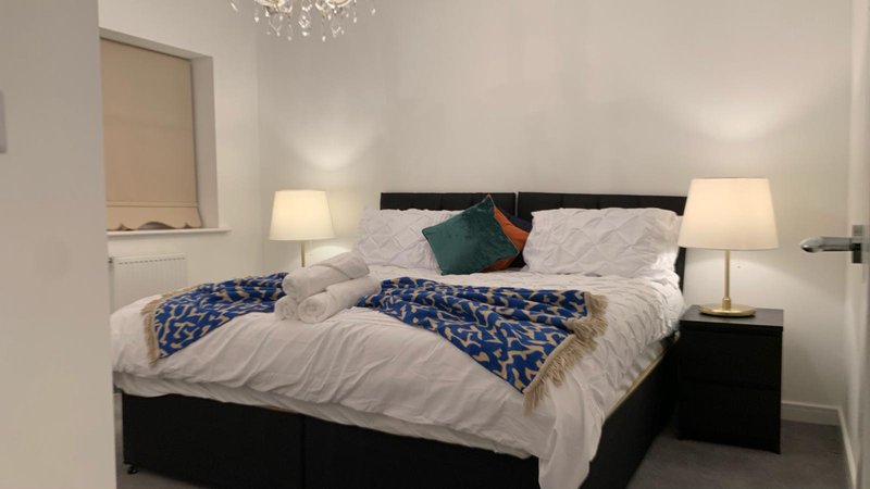 Modern bedroom with double bed, white bedding, blue throw, and bedside lamps