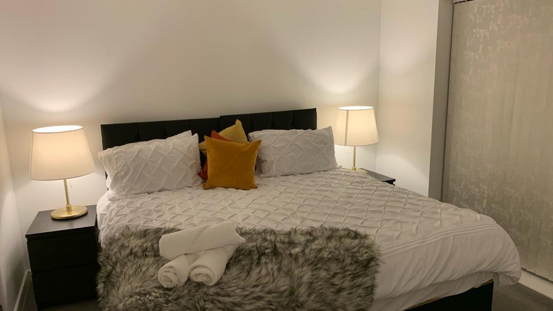 Modern bedroom with queen bed, grey bedding, decorative pillows, and bedside lamps