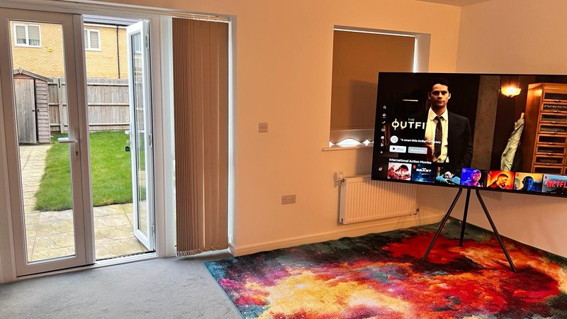 Living room with colorful rug, TV on wall mount, tripod, patio doors to garden
