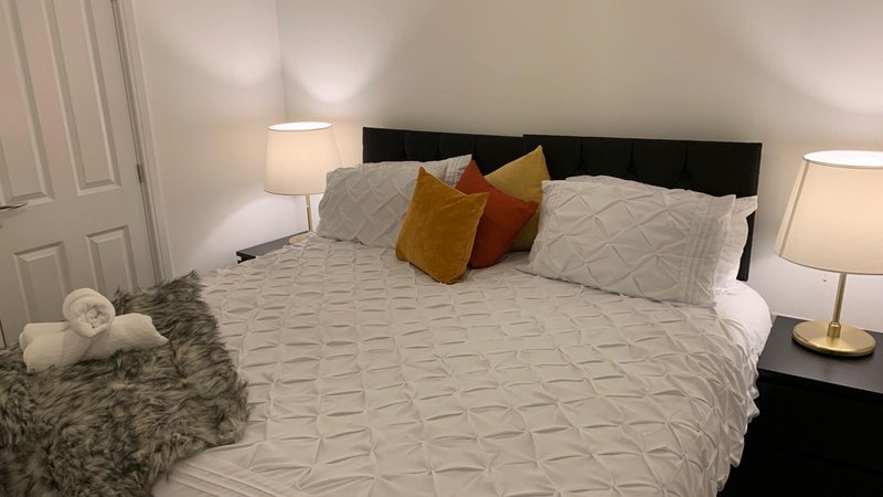 Bedroom with double bed, black headboard, decorative pillows, fur throw, and bedside lamps