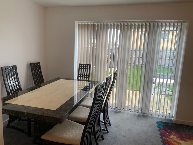 Dining room with wooden table, black chairs, vertical blinds and patio doors overlooking garden
