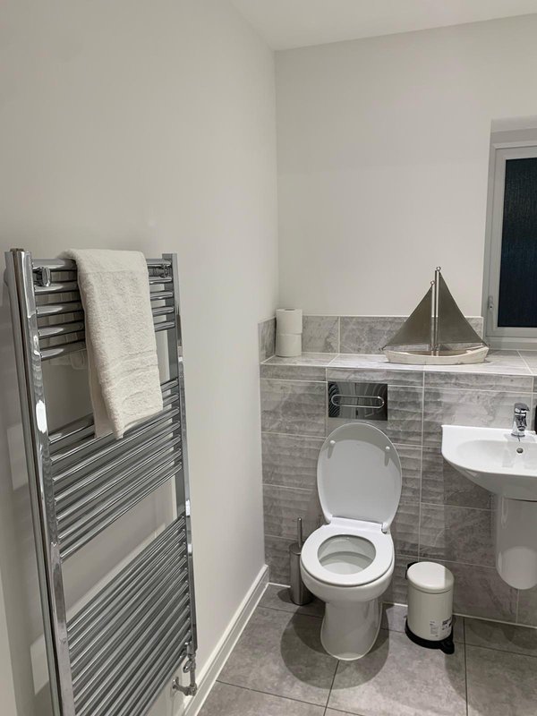 Modern bathroom with toilet, pedestal sink, towel rail and grey tile walls