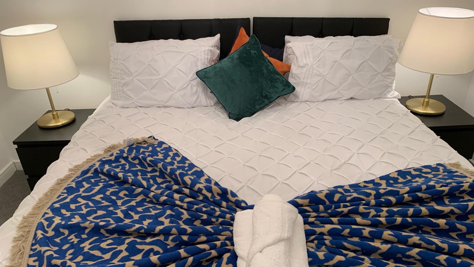 Modern bedroom with queen bed, blue patterned throws, decorative pillows and bedside lamps