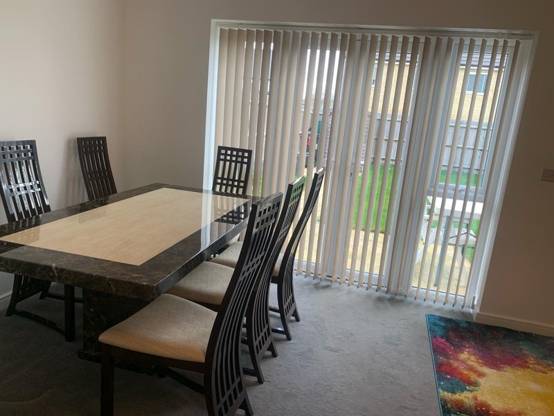 Dining area with wooden table, black chairs, vertical blinds and glass doors to garden