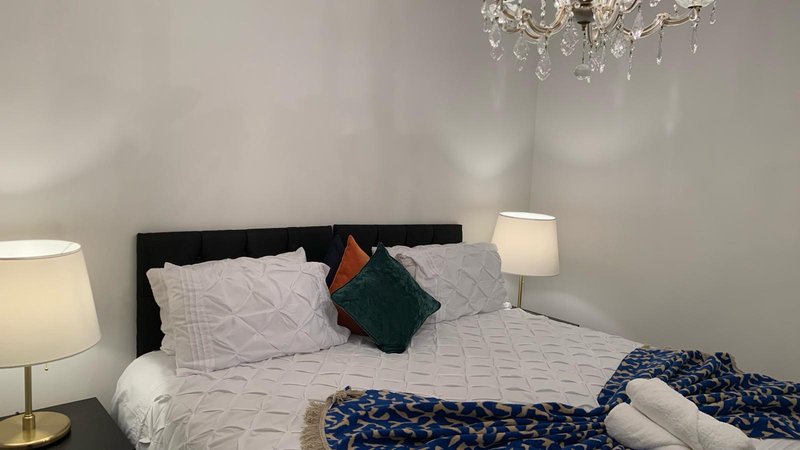 Modern bedroom with double bed, decorative pillows, blue throw blanket, and chandelier overhead