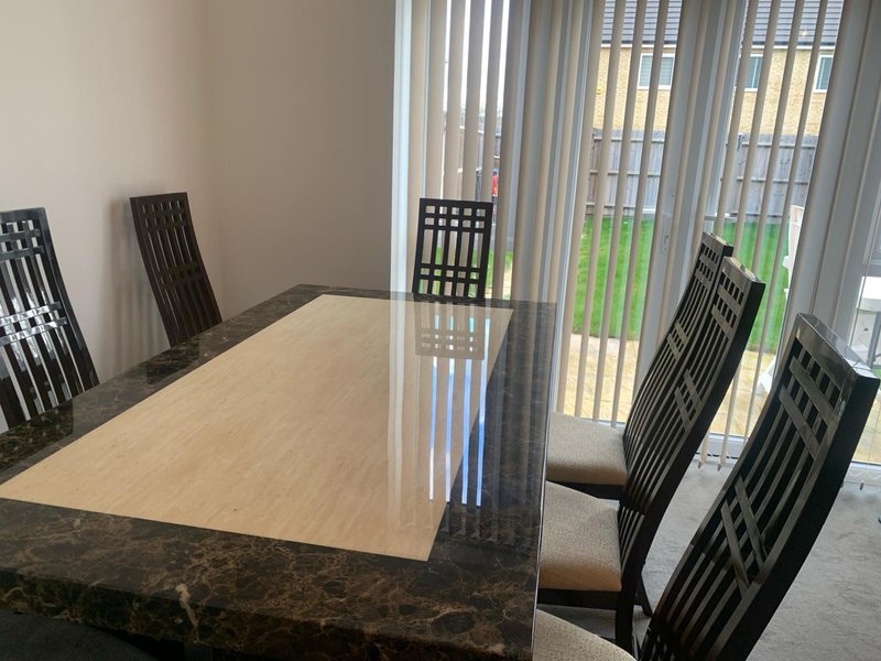 Dining room with wooden table, black chairs, and vertical blinds overlooking garden