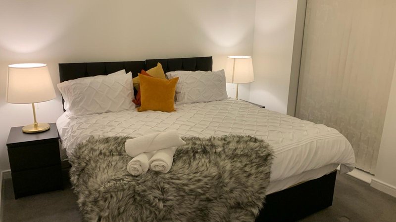 Modern bedroom with black bed frame, white bedding, fur throw, and bedside lamps