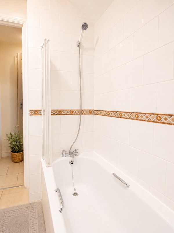 Clean modern bathroom with white subway tiles, bathtub, shower head and decorative border trim