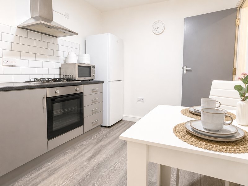 Modern white kitchen with gas cooker, white fridge, island counter and dining setup