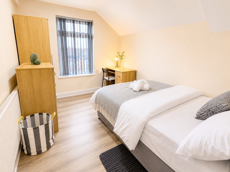 Bright bedroom with two single beds, wooden furniture, window with blinds and light wood flooring