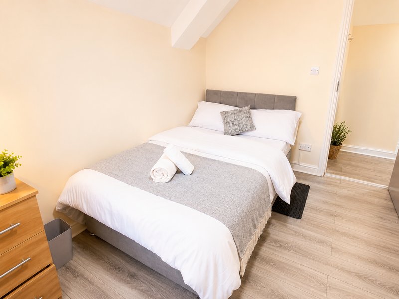Bedroom with double bed, gray headboard, white bedding, wooden dresser and laminate flooring