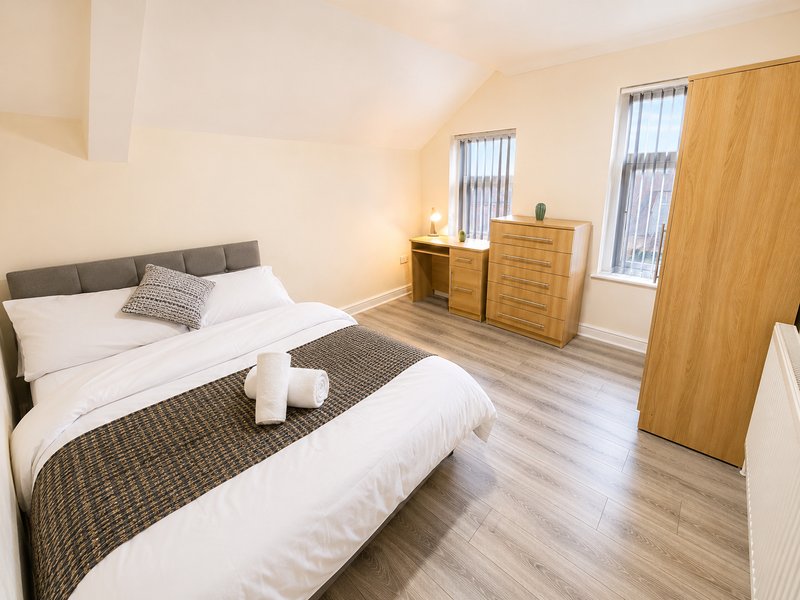 Spacious bedroom with two beds, wooden furniture, and bright windows overlooking street