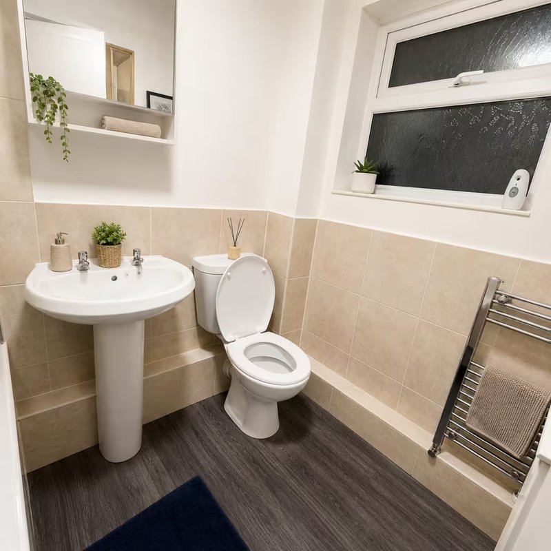 Clean bathroom with pedestal sink, toilet, heated towel rail, and beige tile walls