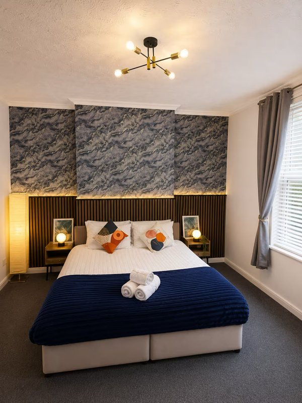 Modern bedroom with blue bed, patterned headboard, bedside lamps and ceiling light fixture