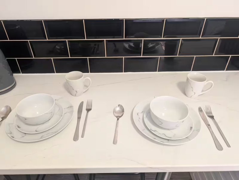 Kitchen counter with place settings, white dishes, cutlery and black tile backsplash