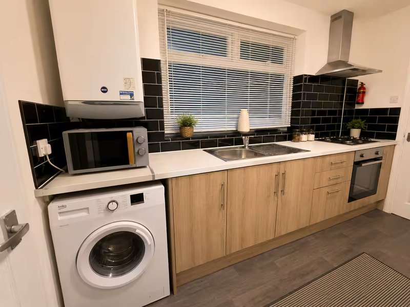 Modern kitchen with wooden cabinets, black tile backsplash, integrated appliances and washing machine