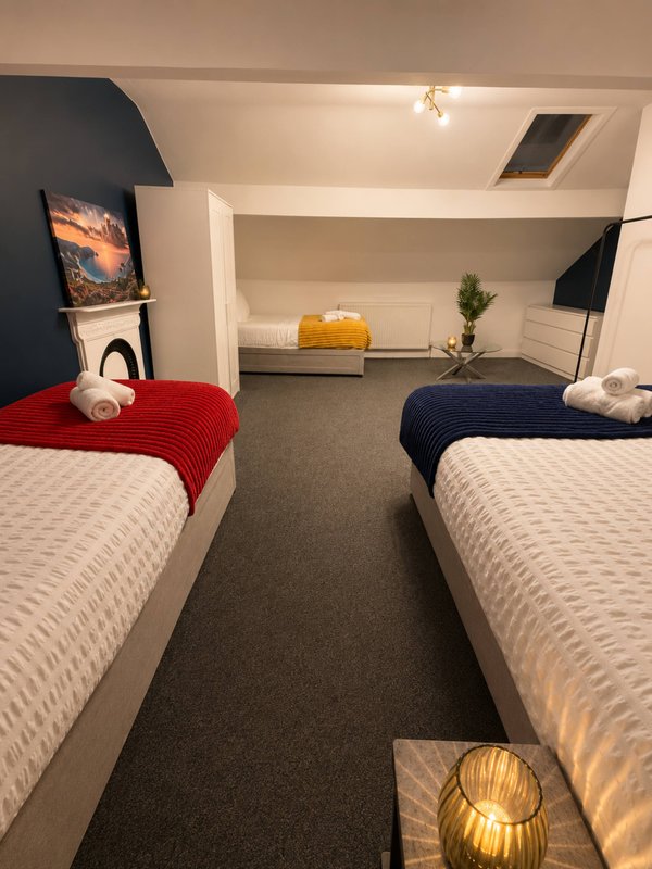 Shared bedroom with two single beds, red and navy blankets, white towels, and decorative cushions