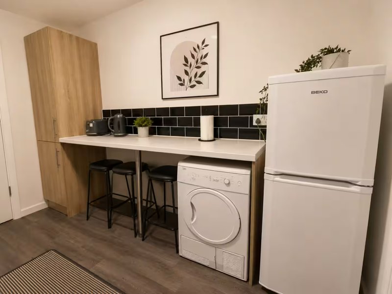 Kitchenette with white appliances, black tile backsplash, wooden cabinetry and bar seating