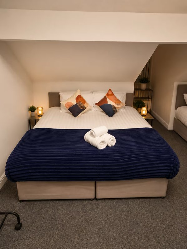 Bedroom with double bed, navy bedding, decorative pillows, white towels, and bedside lamps
