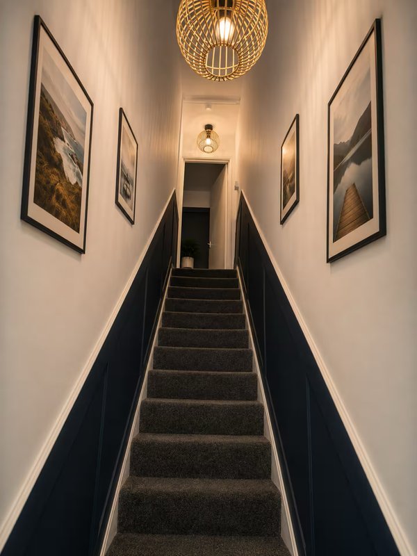 Narrow staircase with dark treads, white walls, framed artwork, and pendant light fixture